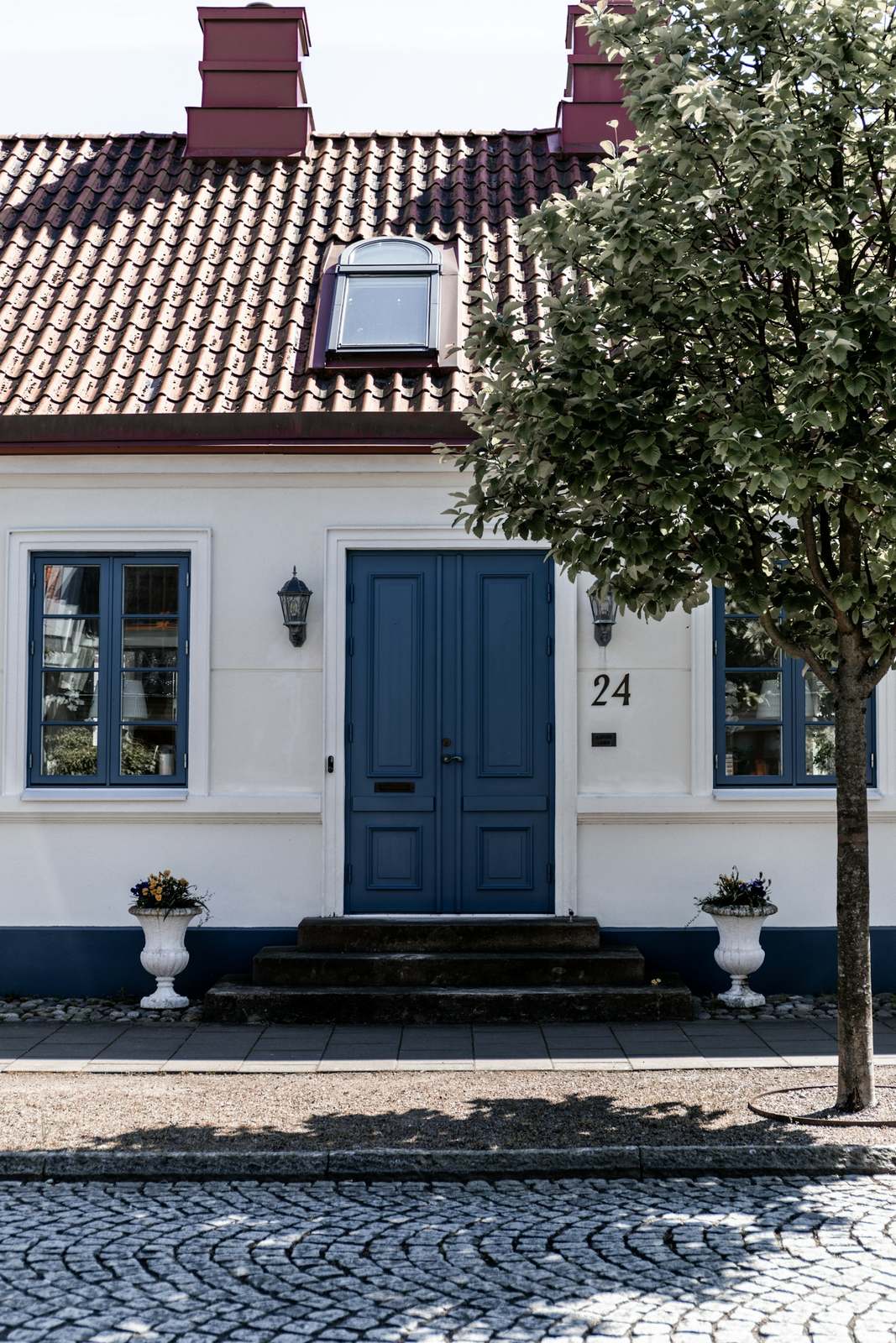 Wit huis met rode dakpannen en een blauwe voordeur aan een kasseistraat